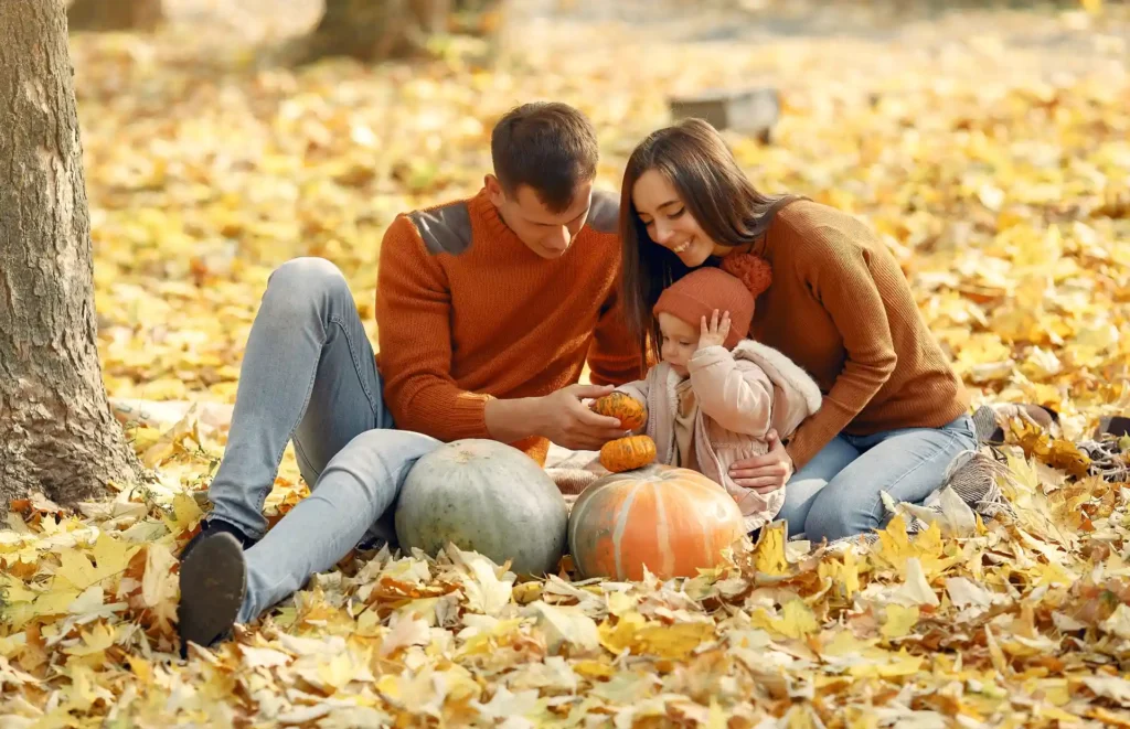 Family Portrait with Baby Girl and Pumpkins in Autumn Leaves