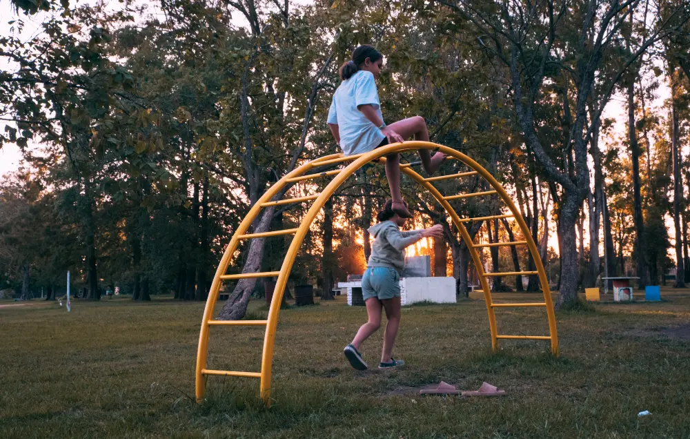 Girls Conquering Yellow Arch Ladder at Sunset