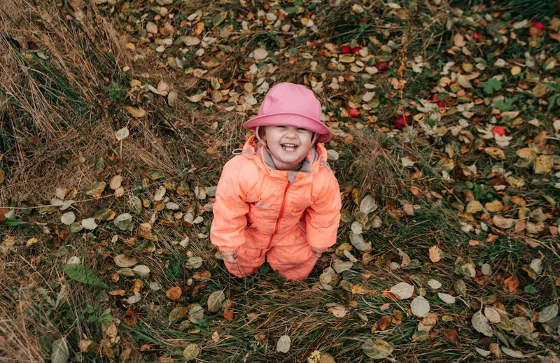 Toddler in Orange Snowsuit Playing in Leaves